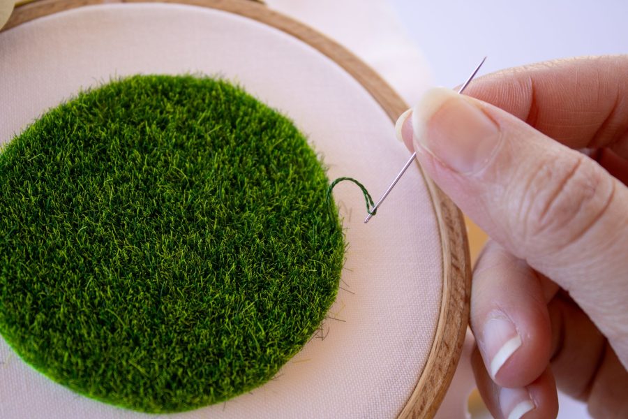 Appliqueing grass on a fabric base with a single strand of cotton thread and an embroidery needle